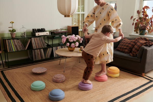 Kind und Erwachsene balancieren gemeinsam auf Trittsteinen im Wohnzimmer und fördern spielerisch Bewegung im Alltag.